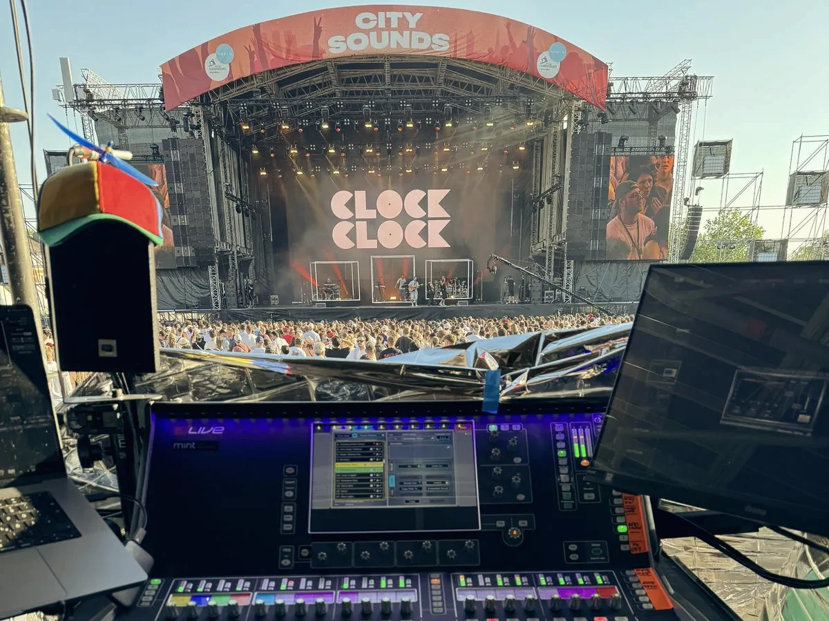 Blick vom FOH-Platz über ein digitales Mischpult auf eine Open-Air-Bühne mit Publikum